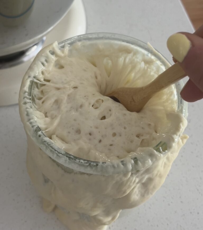 Mixing bubbly, active sourdough starter with a wooden utensil.
