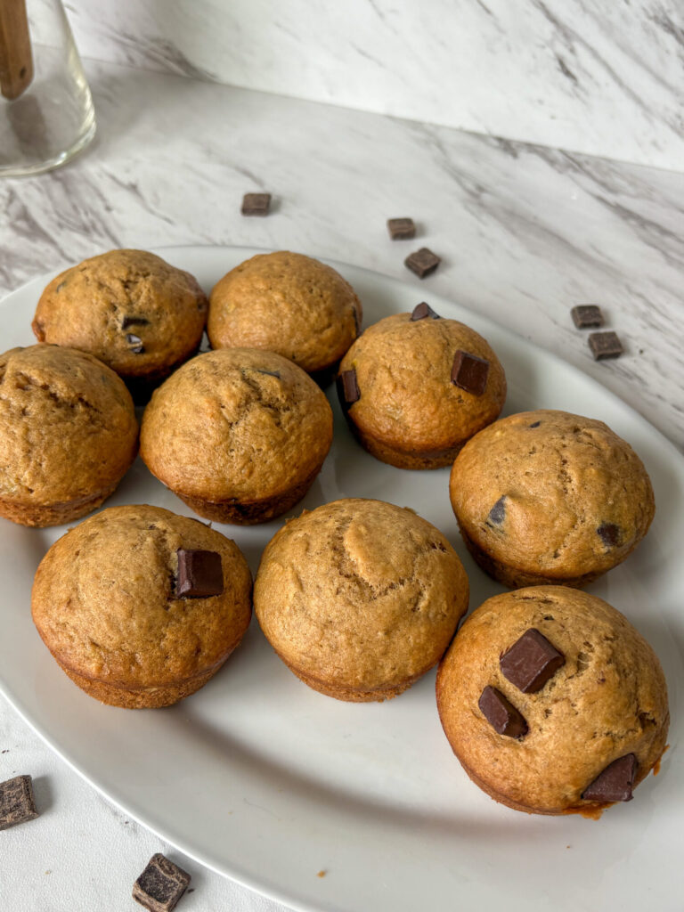 Sourdough discard banana chocolate chip muffins arranged on a white plate with chocolate chunks scattered on marble background.