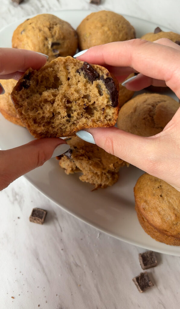 Moist interior of a banana muffin broken open, showing melted chocolate chips and fluffy texture.