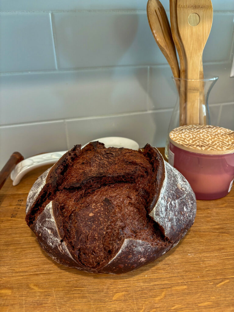 Whole chocolate sourdough bread loaf with deep scoring and a rich, dark crust on a wooden board