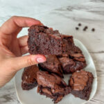 A hand holding a thick, fudgy brown butter sourdough discard brownie with a crackly top and rich chocolate center.