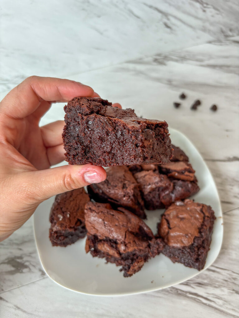 A hand holding a thick, fudgy brown butter sourdough discard brownie with a crackly top and rich chocolate center.