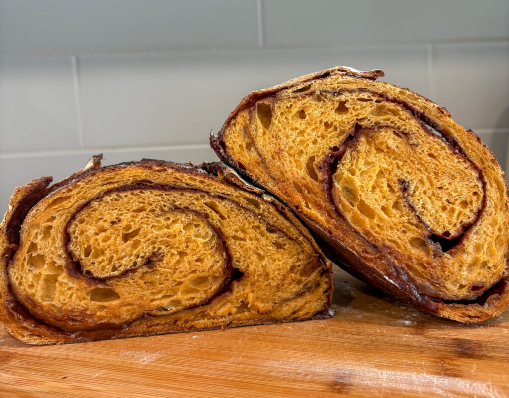 Two halves of pumpkin sourdough bread on a wooden cutting board with visible cinnamon swirl inside.