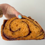 Hand holding a slice of pumpkin cinnamon swirl sourdough bread showing the golden crumb and spiral of cinnamon sugar.