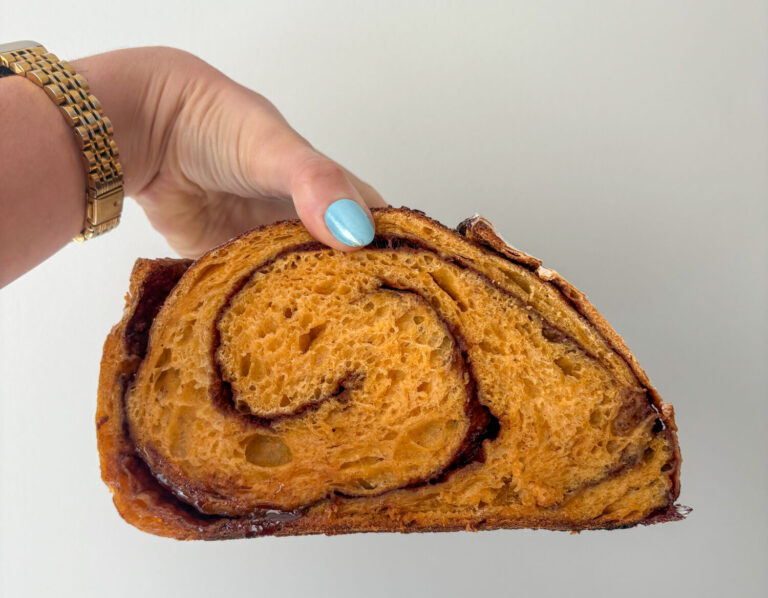 Hand holding a slice of pumpkin cinnamon swirl sourdough bread showing the golden crumb and spiral of cinnamon sugar.